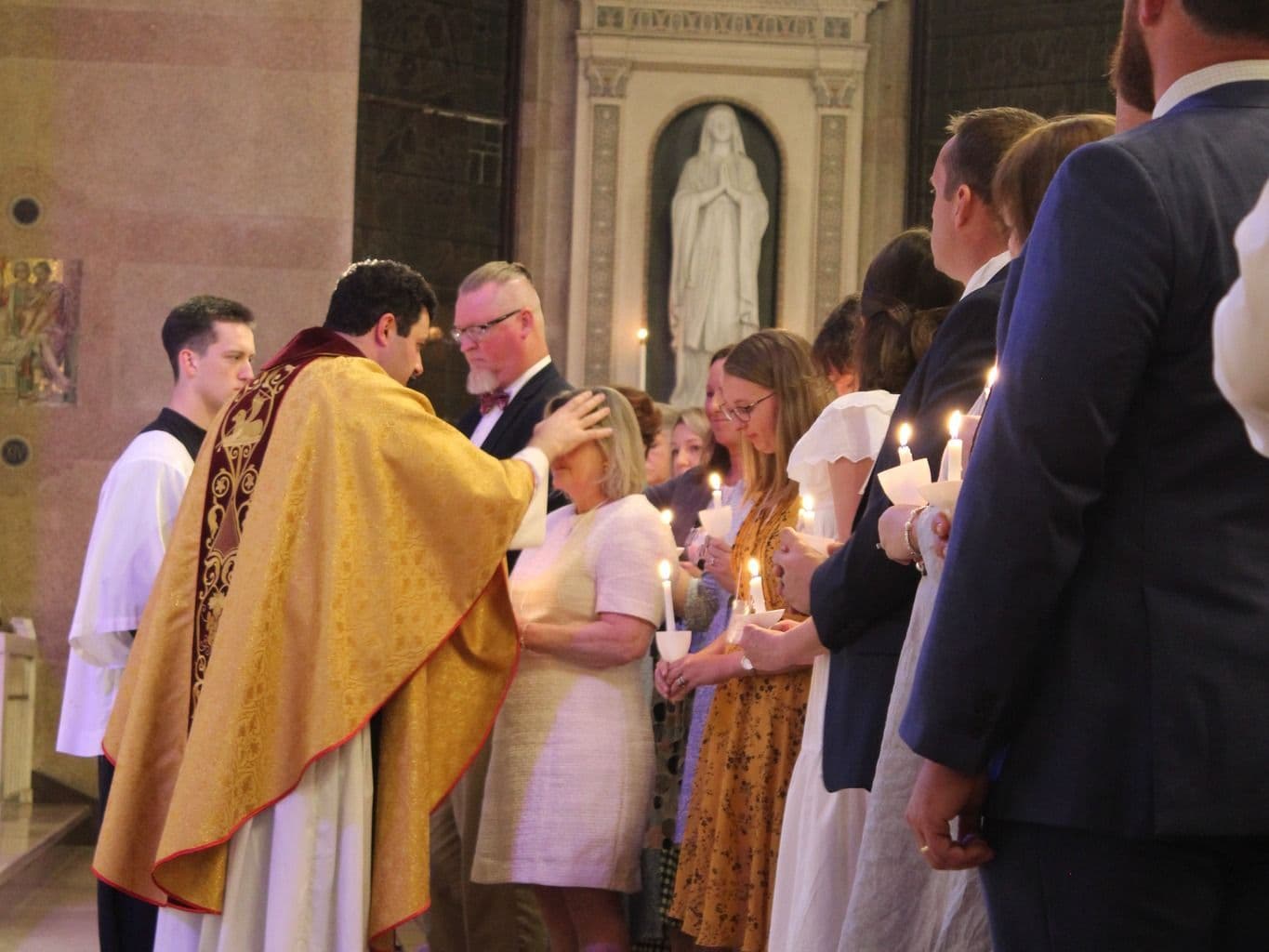 A priest in gold vestments blessing members of the parish who stand holding lit candles during a candlelight liturgy at St. Mary's.
